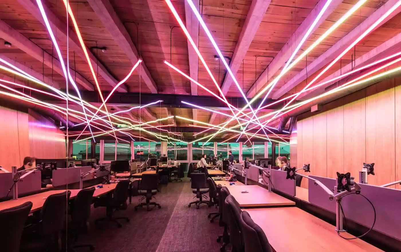 Modern commercial office interior with suspended coloured linear LED lighting creating a layered lighting design across the ceiling