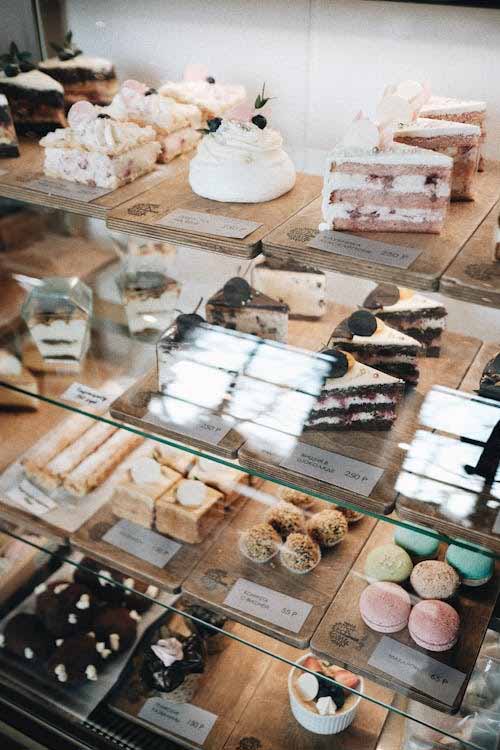 Glass dessert display cabinet with cakes, slices, and macarons lit by internal shelving lighting for clearer product visibility.