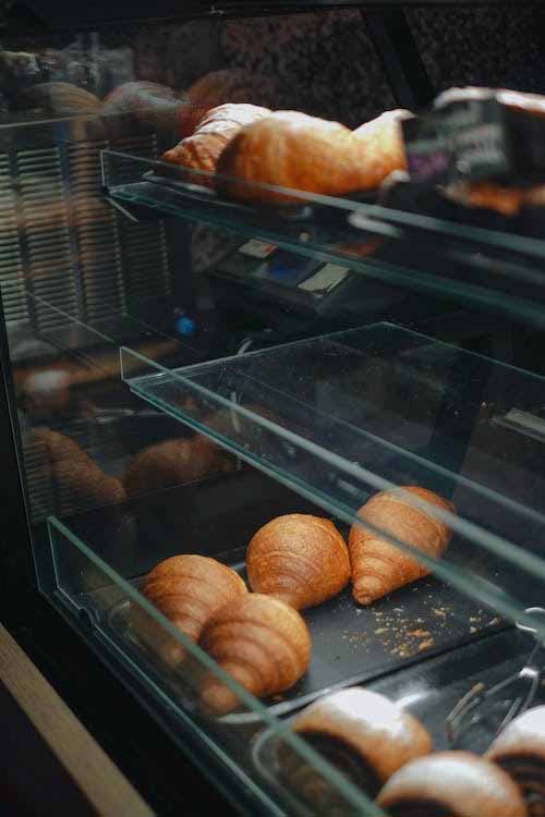 Refrigerated bakery display cabinet with croissants on glass shelves under warm LED cabinet lighting.